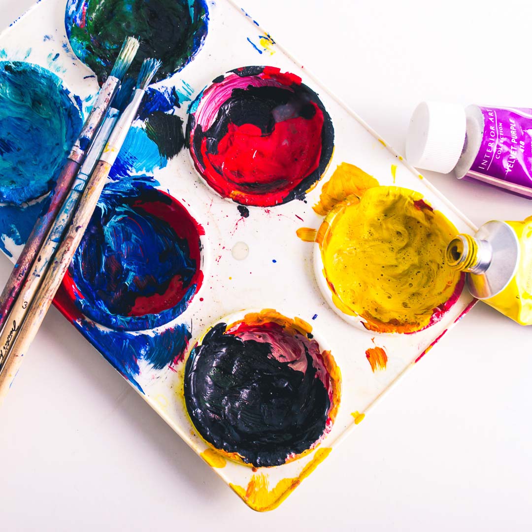 Close up view of a paint pallet filled with paint, surround by used paintbrushes and paint tubes.