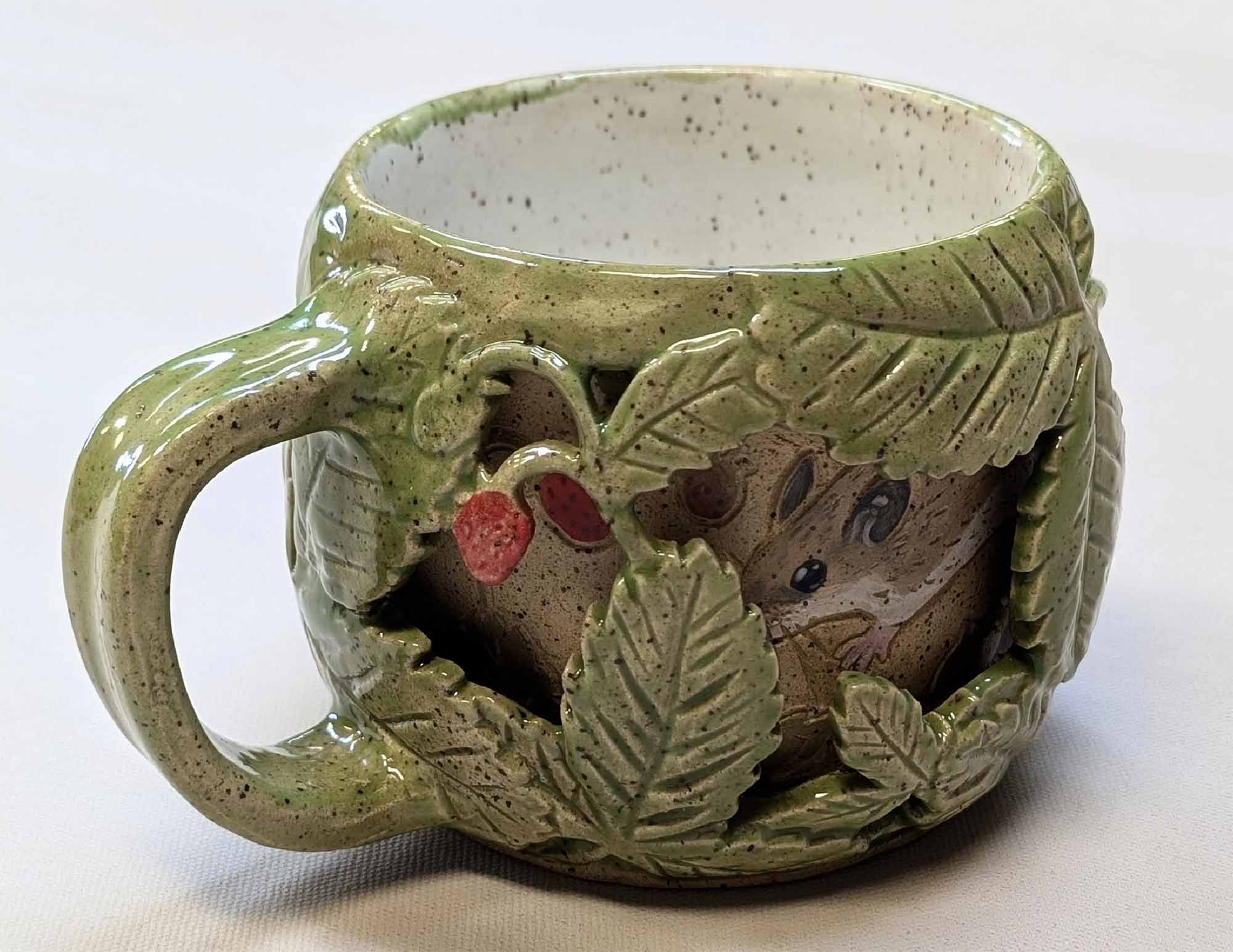 A ceramic mug with a 3d effect of leaves on top and a mouse on the mug layer underneath.